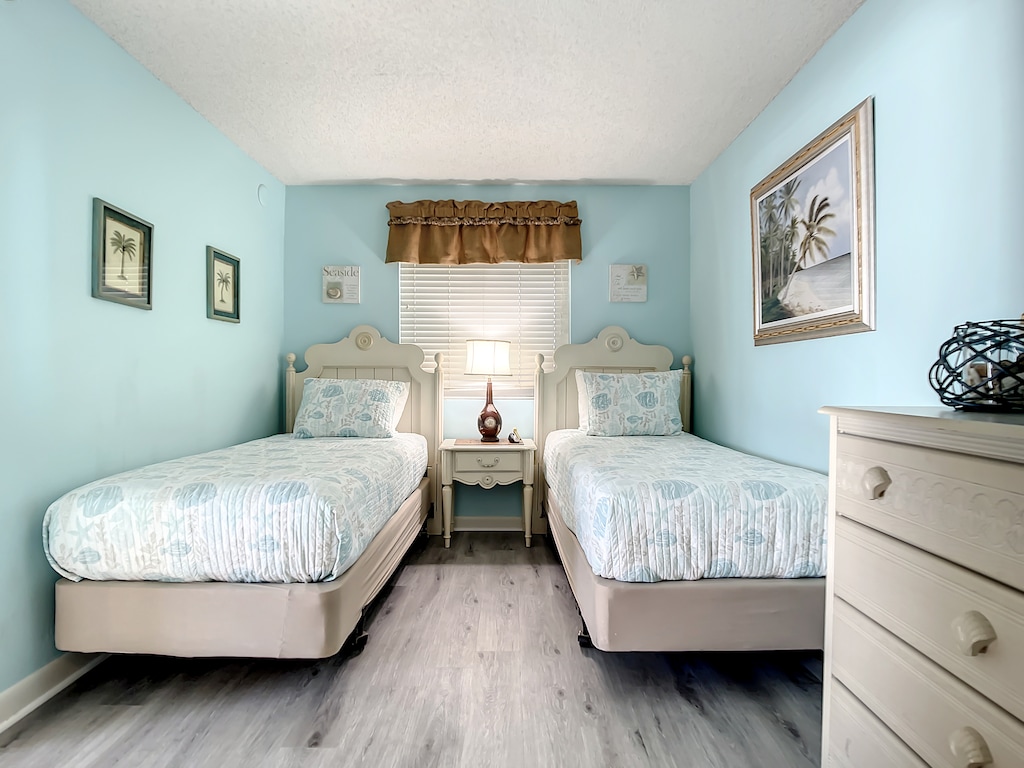 Cozy twin bedroom with soft blue tones, seashell bedding, and beach-themed decor, perfect for a relaxing retreat.