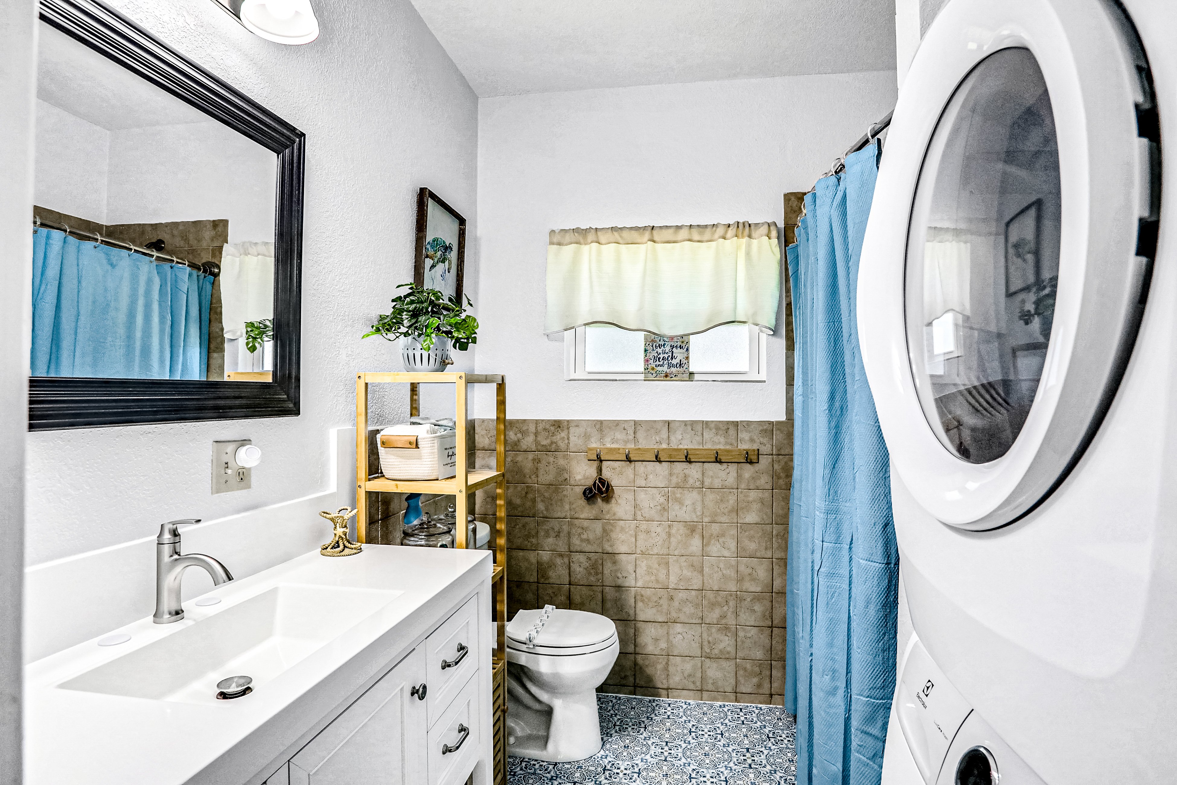Fresh and inviting bathroom featuring beachy blue accents, a spacious vanity, walk-in shower/tub combo, and in-unit laundry—perfect for a relaxing beach stay.