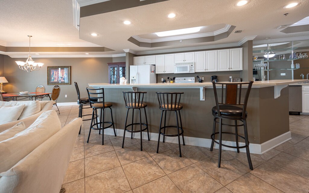 Kitchen bar area with stylish bar seating, a kitchen featuring white cabinetry and appliances and spacious countertops