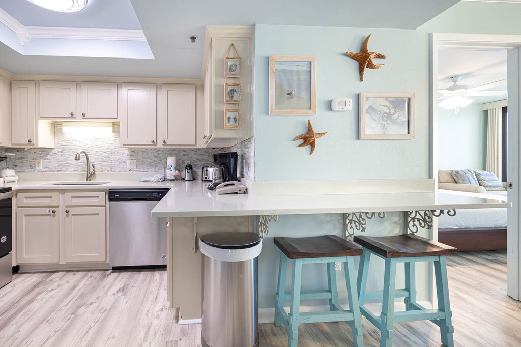 The kitchen features stainless appliances, a breakfast bar with turquoise stools, and beach decor for a refreshing atmosphere