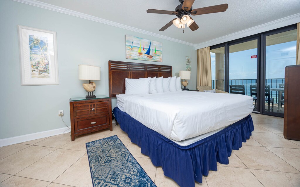 The master bedroom features a large king bed with crisp white linens, coastal decor, and a lovely view from the balcony