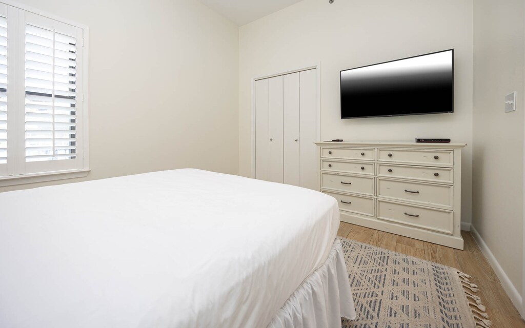 Queen bed, a flat-screen TV mounted on the wall, and a window with plantation shutters in this guest room