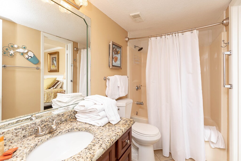 Bright bathroom featuring a granite countertop, neatly arranged towels, and a tub/shower combo with a shower curtain