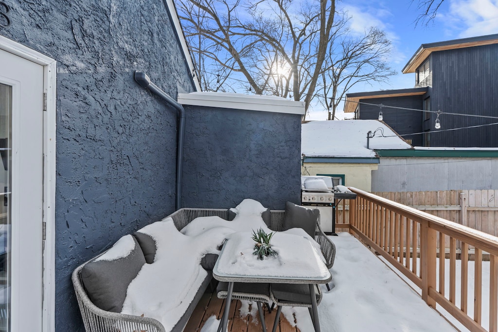 Snow-dusted outdoor patio with modern dining furniture and BBQ setup in a quiet residential neighborhood during winter season.