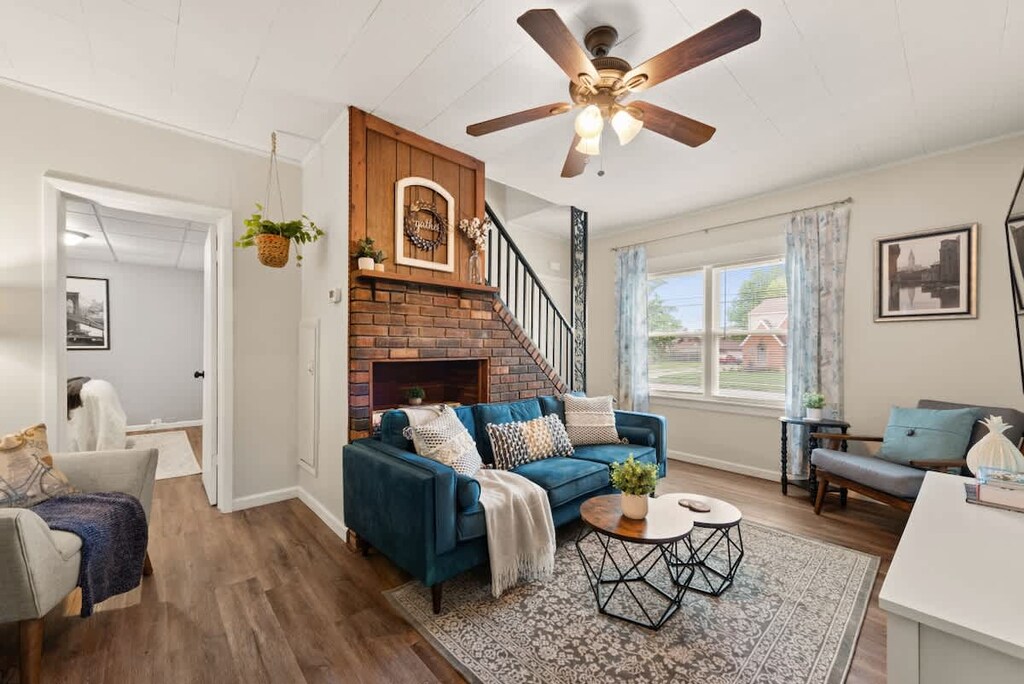 - Bright living space with blue sofa and soft pillows   - Rustic brick fireplace and ceiling fan add comfort   - Large windows bring in natural daylight  