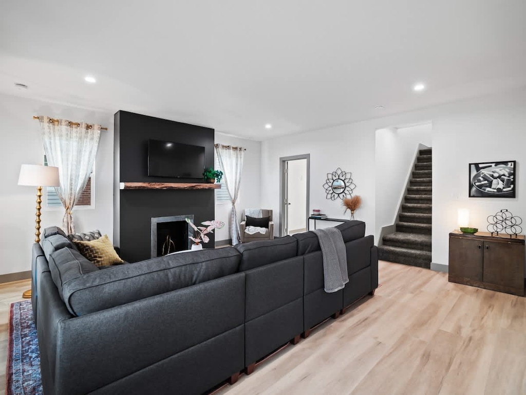 - Living room with large sectional and modern accents   - Flat screen TV above rustic fireplace centerpiece   - Open layout with staircase leading to upper floor 