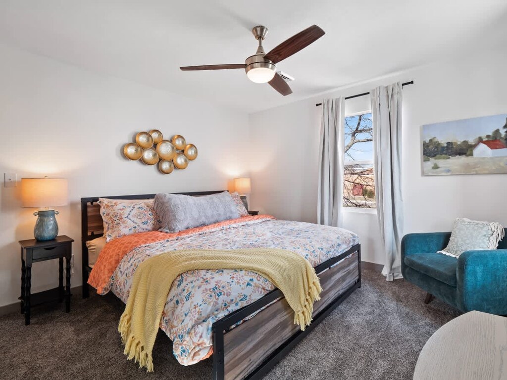 - Bedroom with king bed and floral bedding design   - Ceiling fan and cozy armchair by window view   - Soft lighting with nightstands and relaxing retreat  