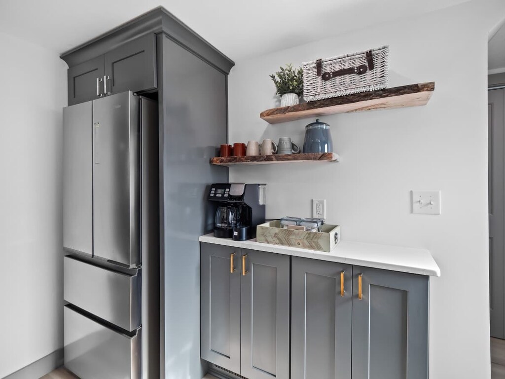 - Stainless steel fridge with bottom freezer design   - Coffee maker with mugs and floating wood shelves   - Modern cabinetry with gold handles and storage space  