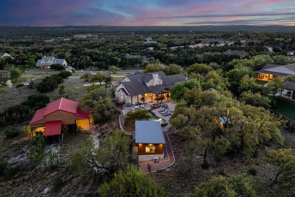 Stunning aerial view showcases the property nestled among rolling hills and native trees in a peaceful residential setting.
