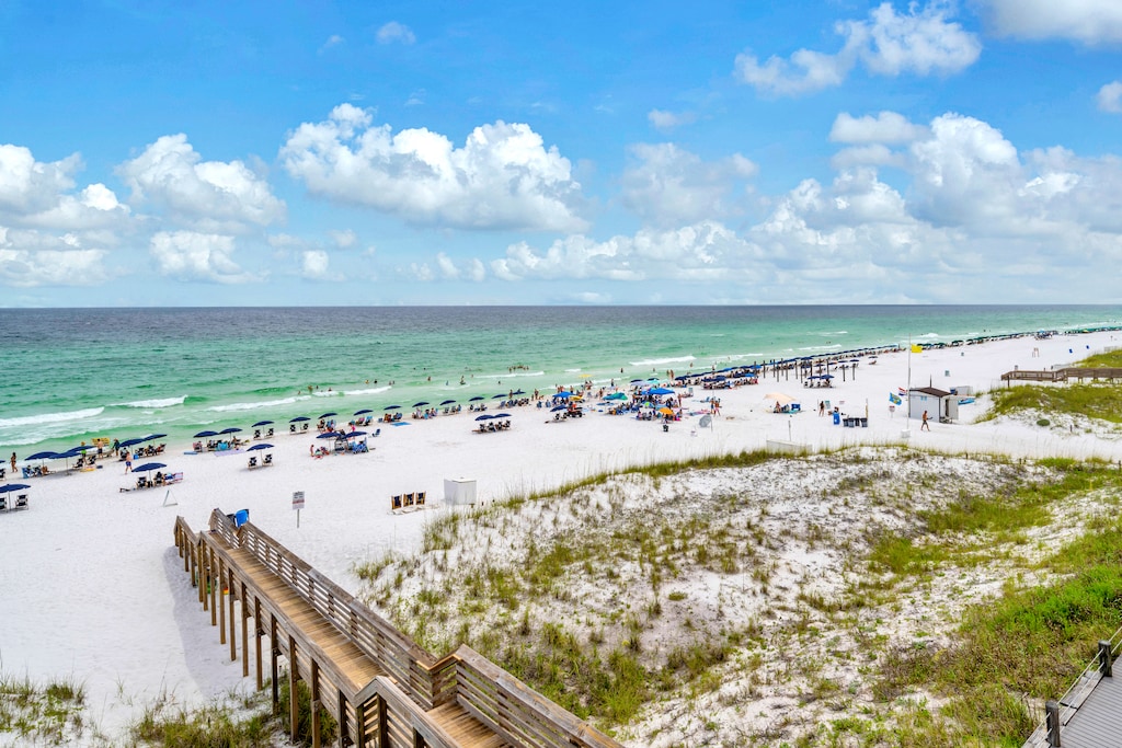 Pristine white sand beach with emerald waters stretches endlessly along the coast, featuring beach access boardwalk and natural dune preservation.