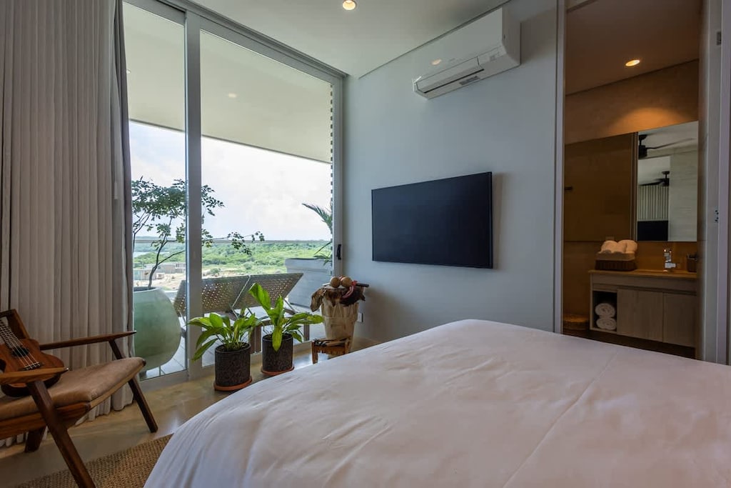 - Bright bedroom with panoramic balcony views  
- TV setup and cozy decor for a peaceful stay  
- Natural light and soft tones create a relaxing retreat