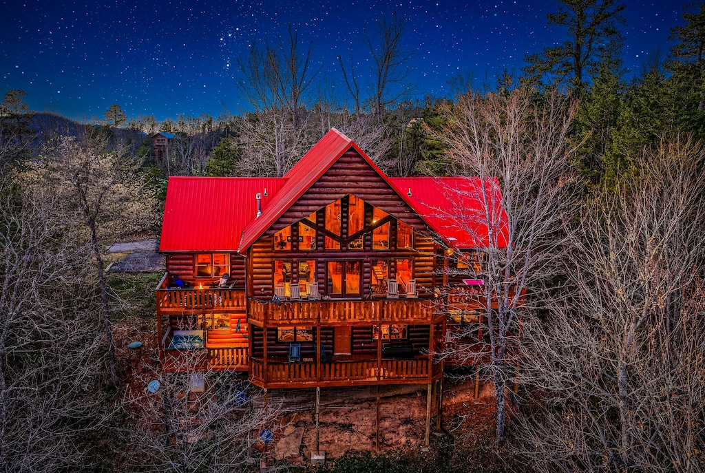 Stunning log cabin retreat glows warmly against a starlit mountain sky, surrounded by peaceful forest landscape.