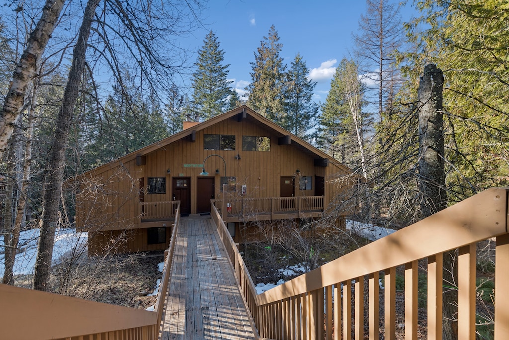 A welcoming wooden cabin nestled among towering evergreens, connected by a charming boardwalk through the peaceful forest setting.