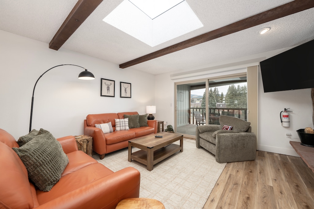 Unwind in this stylish living room featuring exposed beams, a cozy fireplace, and natural light from the skylight above.