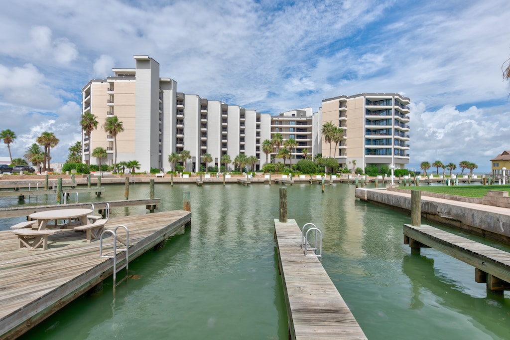 Waterfront condo complex with private marina and boat slips, surrounded by palm trees along the shore.