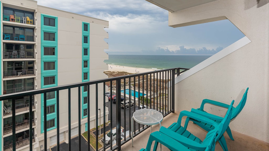 Enjoy a relaxing view of the beach from the balcony, featuring turquoise chairs and a small table for outdoor comfort