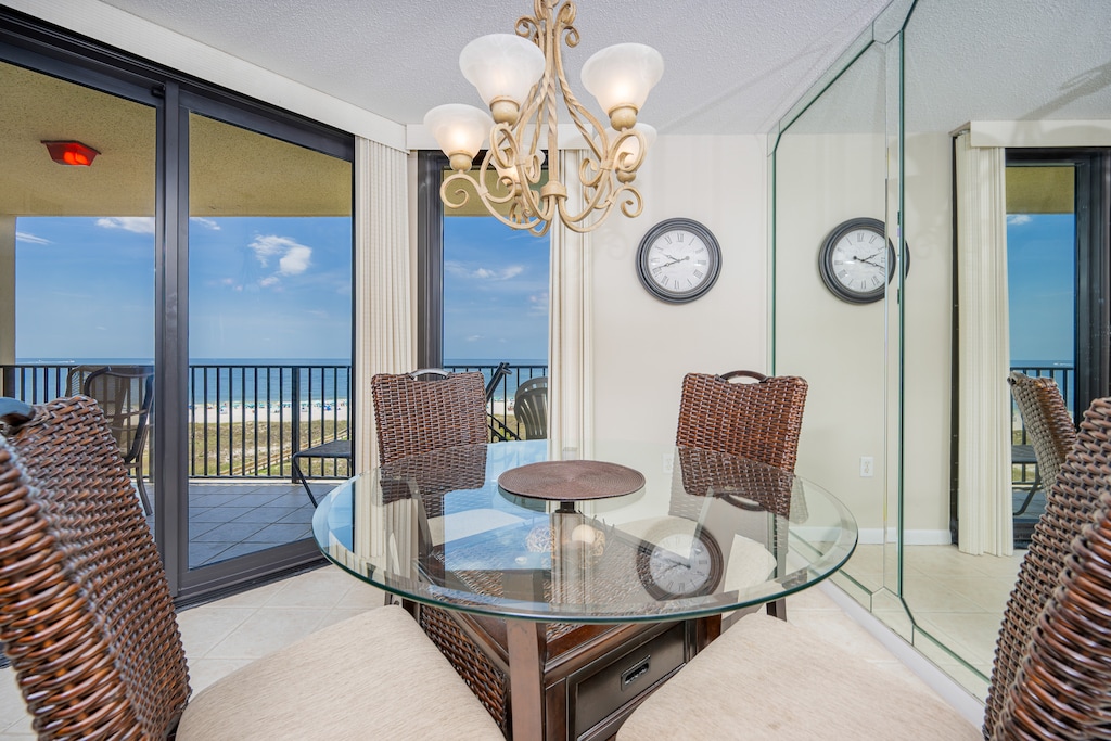 Dining area features a round glass table with woven chairs, offering a view of the beach through sliding glass doors