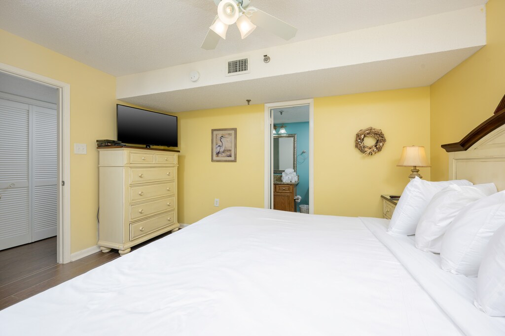 The bright yellow bedroom features a king bed, a TV mounted above a dresser, and an ensuite bathroom