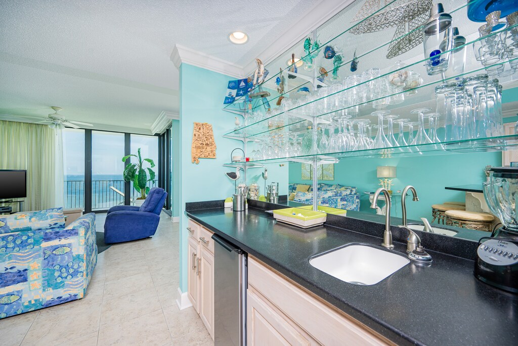 Enjoy a refreshing drink at the sleek wet bar area, surrounded by vibrant decor and glassware, with an ice maker