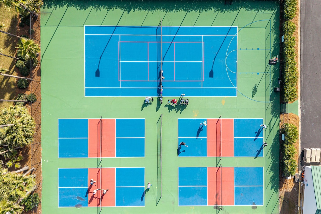 Aerial view of vibrant tennis courts and multi-sport facilities surrounded by tropical landscaping, offering active guests recreational options.