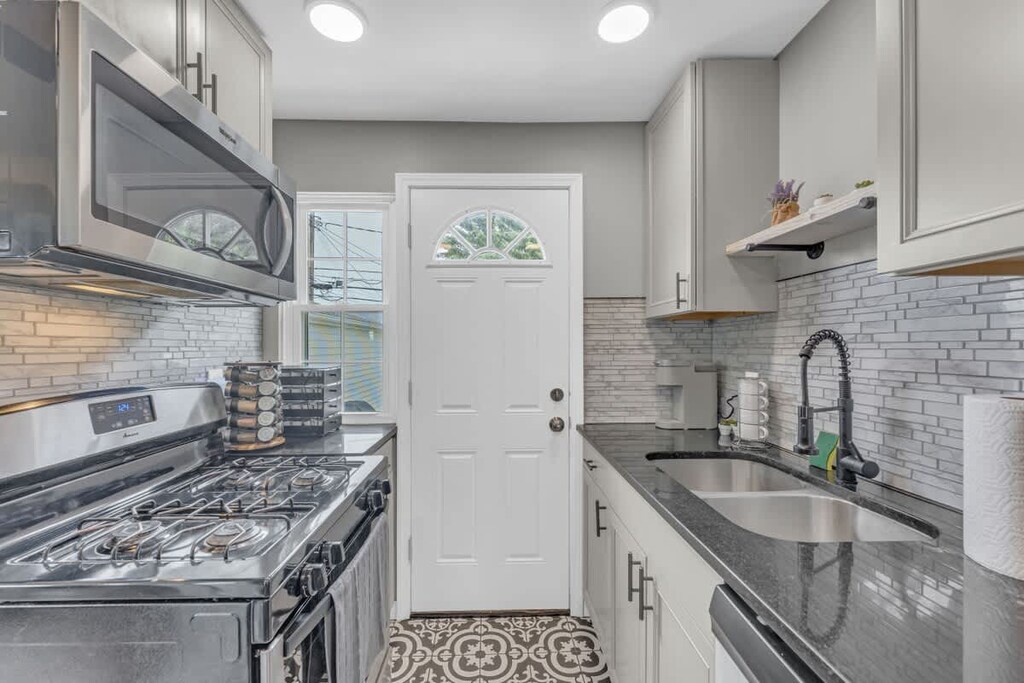 - Sleek galley kitchen with double sink and fresh cabinetry   - Stainless steel appliances and modern fixtures throughout   - Bright space with window and door leading to backyard  
