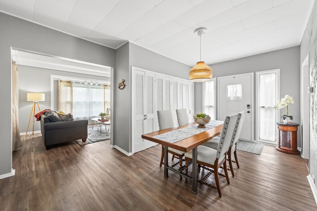 Bright dining area showcases a live-edge wooden table with a lace runner, surrounded by white upholstered chairs and topped with a bowl of green apples. A woven pendant light hangs above, while a row of white louvered closet doors lines the gray wall