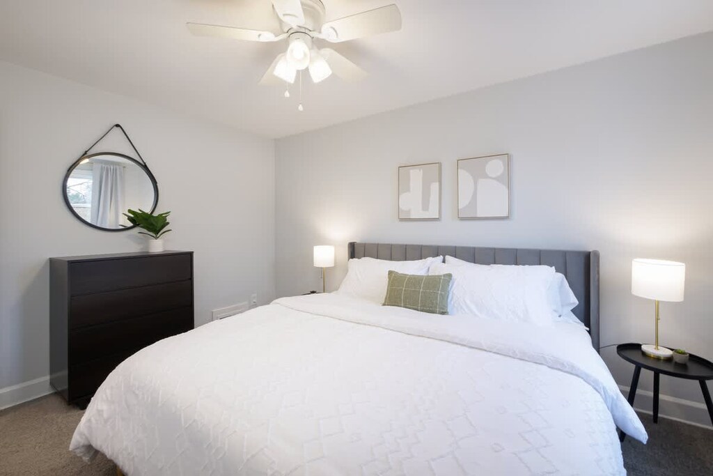 - Bedroom with king bed and cozy white linens   - Modern decor with dresser, mirror and plant accents   - Ceiling fan and lamps provide comfort and lighting  