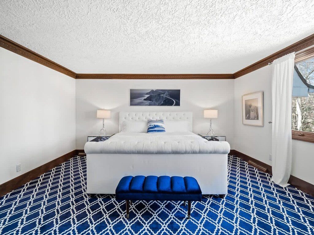 Spacious suite with striking royal blue carpet, a plush white bed, and modern chrome accents. The clean lines and bold pattern create a crisp, upscale retreat.