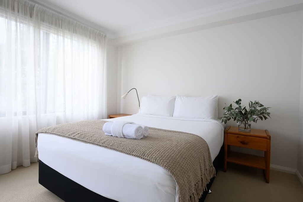 Drift into a peaceful sleep in our comfortable bedroom. Featuring plush pillows, convenient bedside tables, a calming plant, a reading lamp, and fresh towels for your comfort.