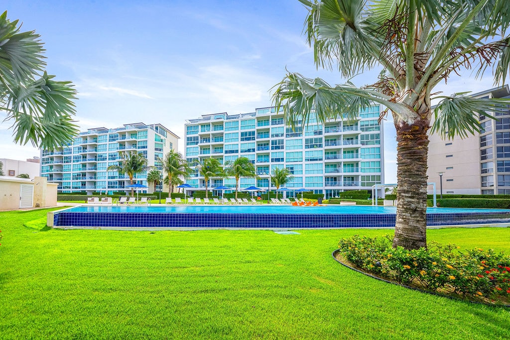 Modern beachfront resort complex featuring contemporary architecture with palm trees and manicured grounds in a tropical setting.
