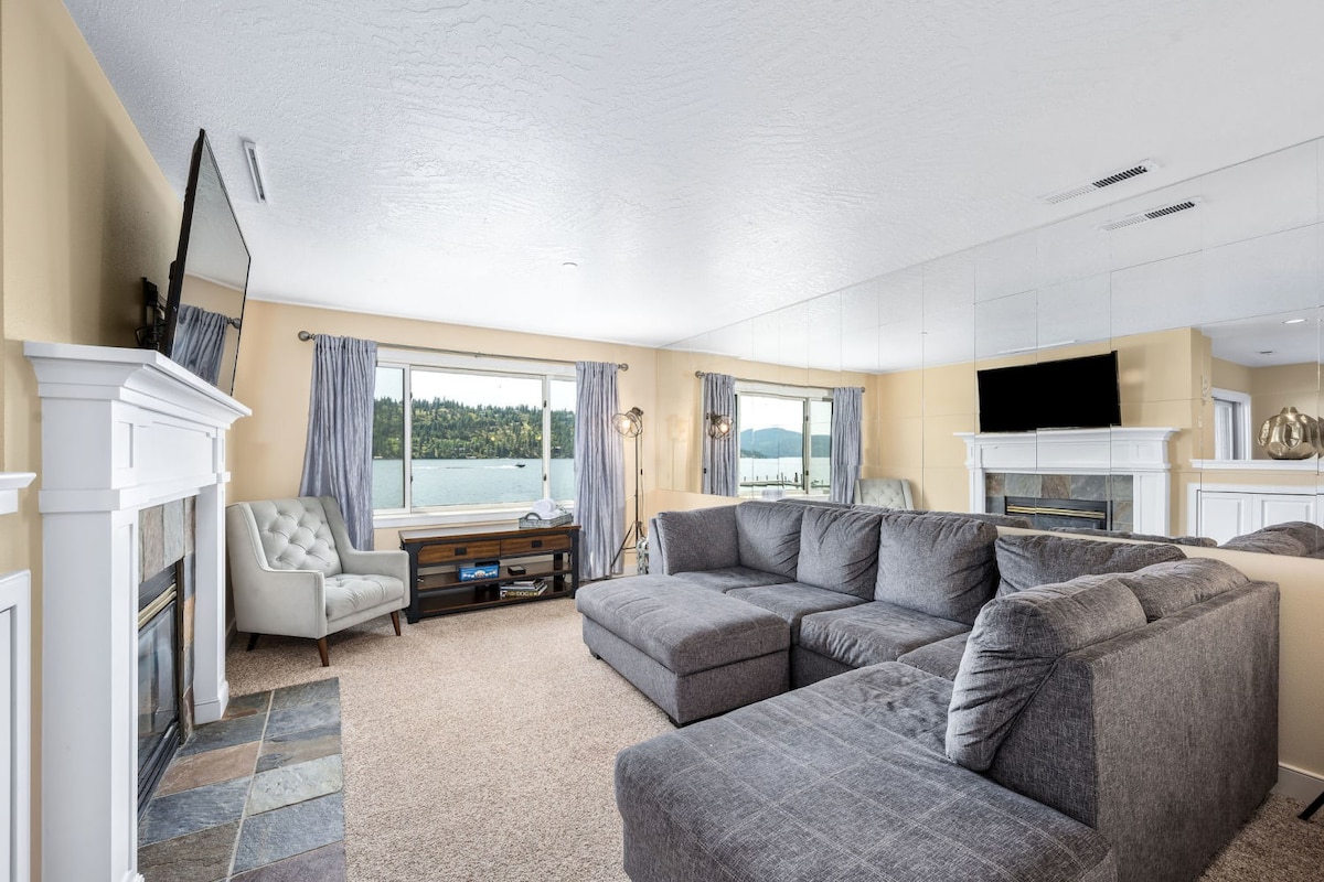 Unwind in this spacious living room featuring a plush sectional sofa, cozy fireplace, and stunning lake views through large windows.