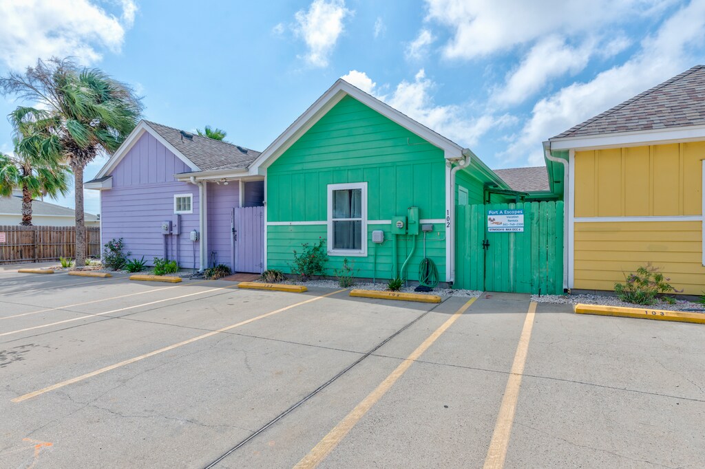 Colorful beach cottages create a cheerful arrival experience with convenient parking spaces and tropical palm trees setting the coastal scene.