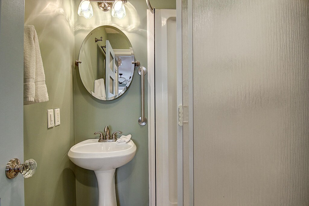 Step into your elegant powder room featuring a classic pedestal sink, round mirror, and thoughtfully designed lighting for your comfort.