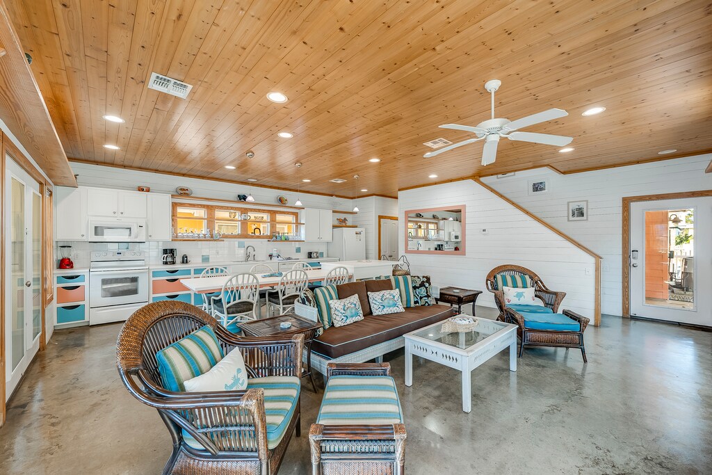 Your open-concept living space features vaulted wood ceilings, coastal wicker seating, and a fully equipped kitchen where you'll create memorable vacation meals.