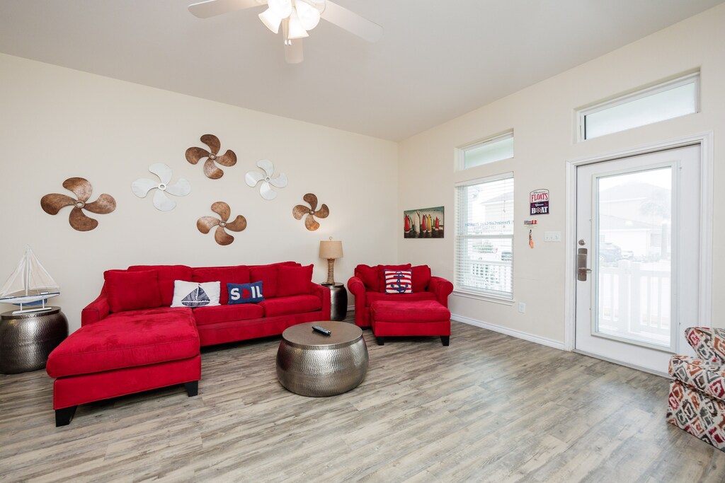 Sink into vibrant red sofas in your nautical-themed living room, where ceiling fans create gentle breezes and balcony doors open to fresh air.