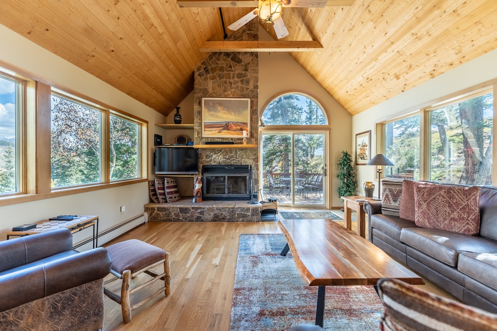 Unwind in your spacious living room with soaring ceilings, stone fireplace, and panoramic windows framing serene forest views.