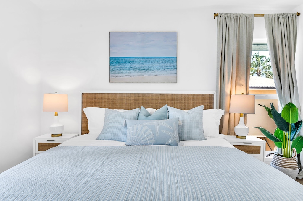 The primary bedroom suite is coastal "Serena & Lily" inspired. The king bed is a mango wood platform bed with a woven cane head and footboard in a natural finish, topped with a LUCID aloe gel memory foam mattress and 100% luxurious cotton linens.