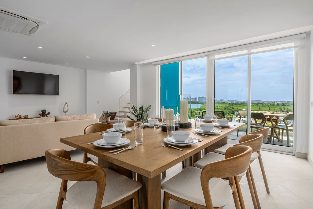You'll love gathering around this elegant dining table, set for six with modern dinnerware and bathed in natural light streaming through floor-to-ceiling windows that frame stunning green views beyond.