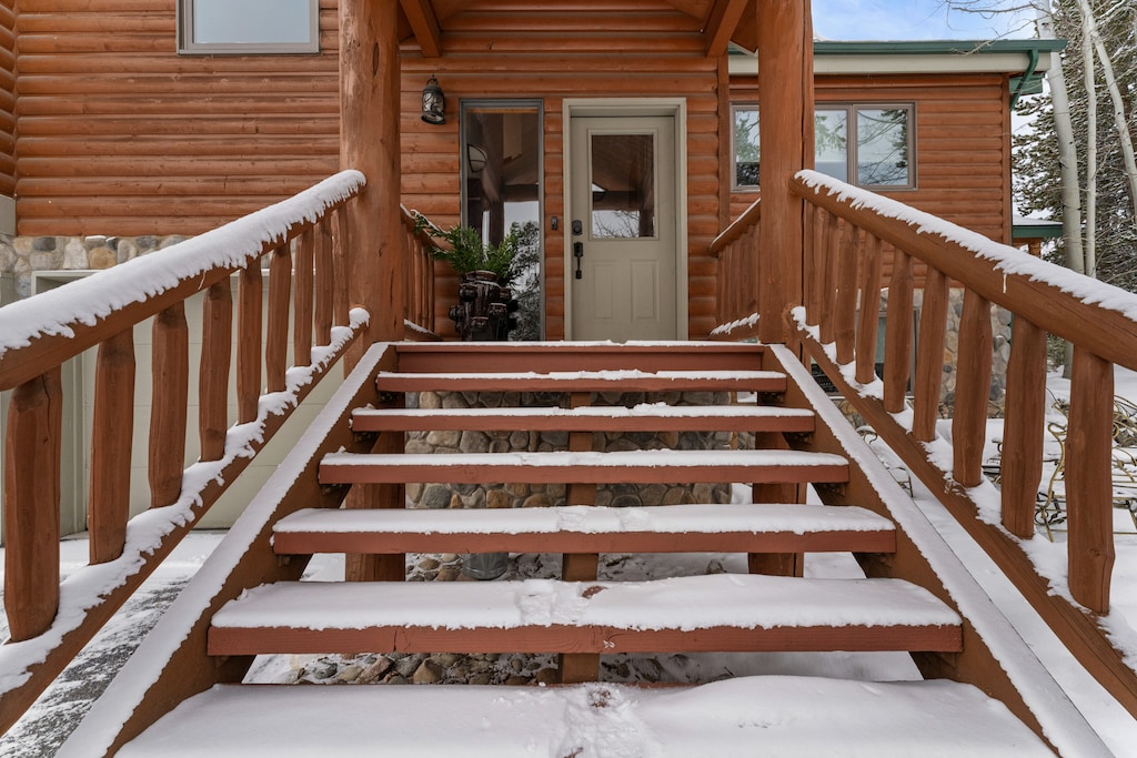 Snow-dusted wooden steps lead to the welcoming entrance of this charming log cabin retreat.