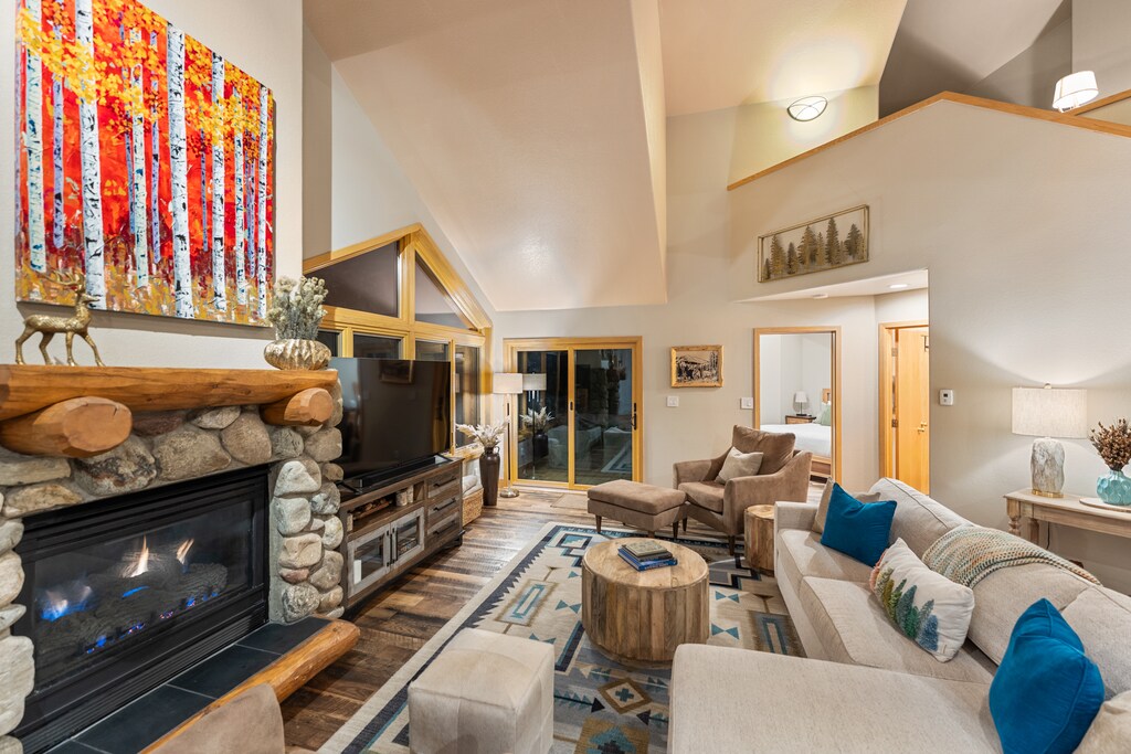 Cozy up in this spacious living room featuring a stunning stone fireplace, plush seating, and vibrant artwork to create your perfect mountain retreat atmosphere.