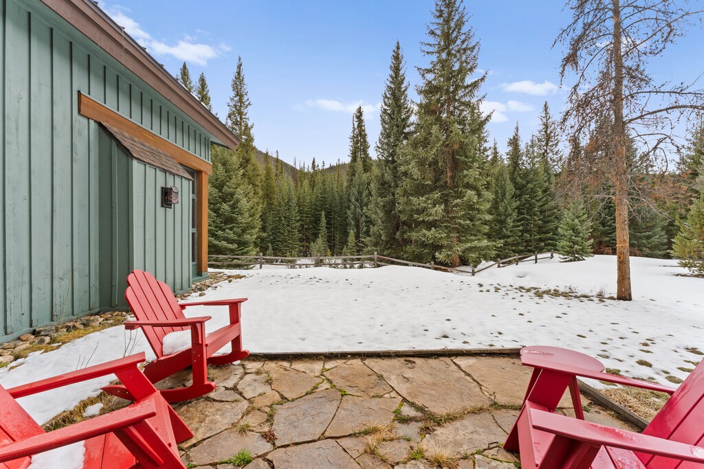 Charming mountain cabin with red Adirondack chairs on stone patio, surrounded by pristine forest and snow-dusted grounds.