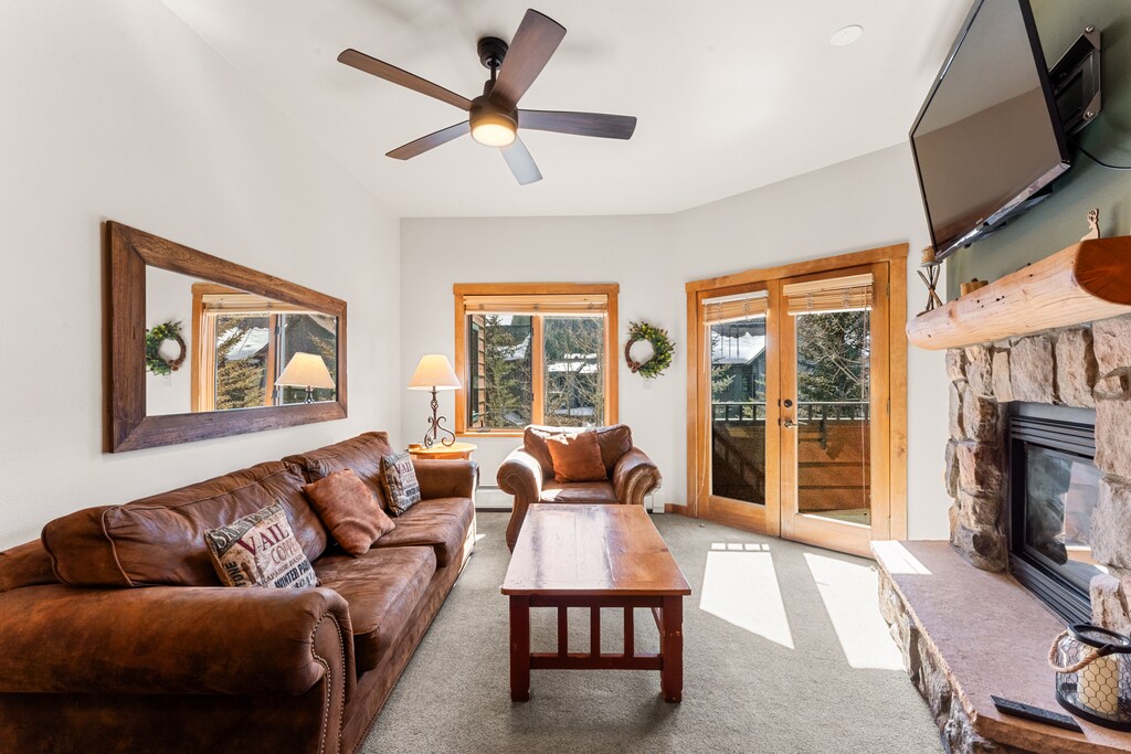Unwind in your cozy living room with rich leather seating, crackling stone fireplace, and mountain views through expansive windows.